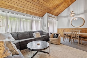 Ein gemütliches Wohnzimmer mit einer Eckcouch, einem runden Couchtisch, einem Holzessttisch mit Stühlen und einer Decke mit Holzbalken.