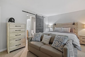 Ein Schlafzimmer mit einem Bett, einem Schminktisch, einem Schlafsofa und einer Schiebetür im Bauernhausstil.