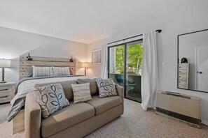Ein Schlafzimmer mit einem Bett, einem Schlafsofa, einem Nachttisch, einer Lampe, einer Schiebetür und einem Spiegel.