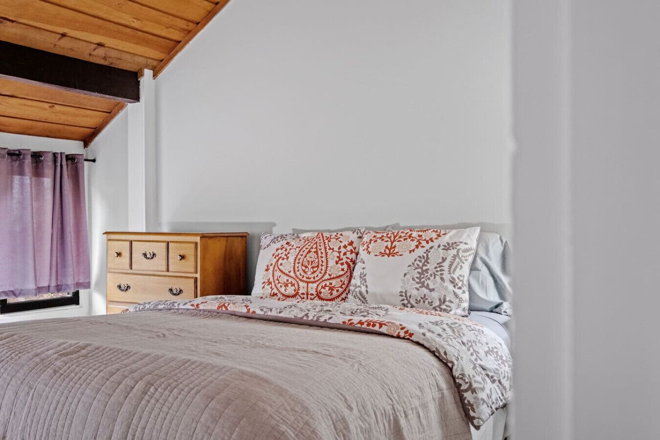 A bedroom with a bed, a wooden nightstand, and a window with curtains.