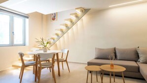 Ein modernes Wohnzimmer mit Treppe, einem Essbereich mit Holzstühlen und einem weißen Tisch sowie einem Sofa mit Beistelltisch.