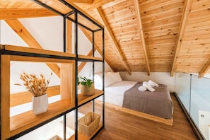 A bedroom with a sloped ceiling, wooden beams, a bed with white linens, a bedside table with a plant, and a window. - Neilis - Modern Retreat in Central Kalamata (Kalamata)
