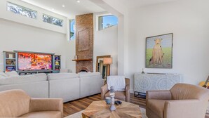 Een moderne woonkamer met een grote televisie, een open haard, een bank en een schilderij aan de muur.