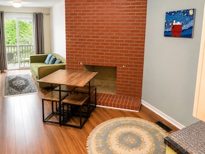 Una habitación con chimenea de ladrillo, un sofá verde, una mesa de madera y una alfombra estampada.