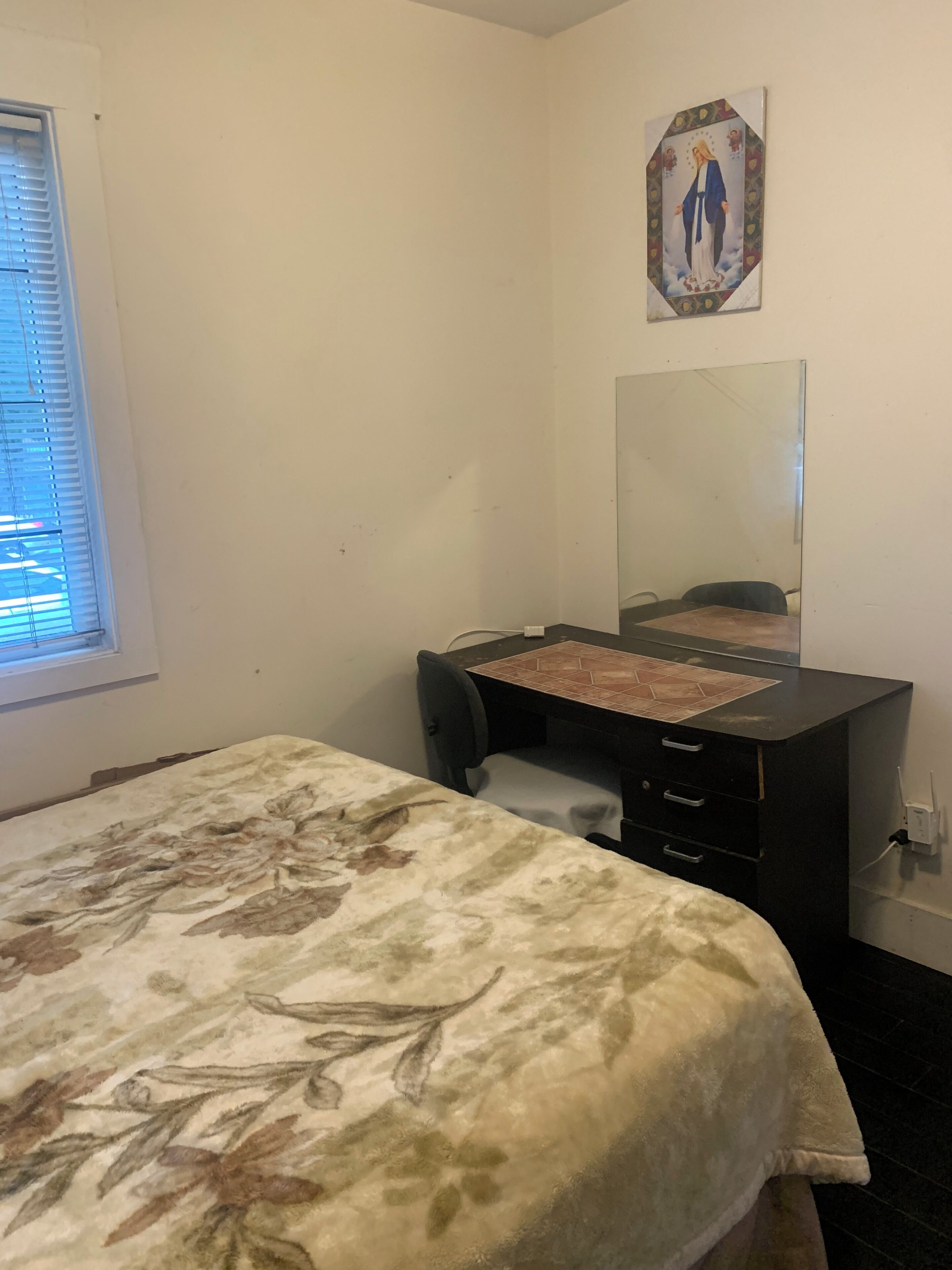 A bedroom with a bed, a desk, a chair, a mirror, and a window.
