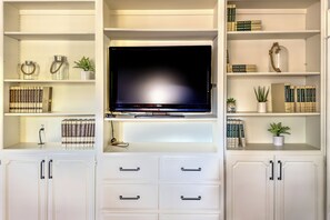 Ein Wohnzimmer mit Flachbildfernseher auf einem Schrank, umgeben von Bücherregalen und Dekoration.