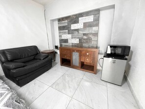 A living room with a black leather sofa, a wooden cabinet, and a white refrigerator. - Depto. Puente Internacional 
Alojamiento entero vivienda rentada en Reynosa Méx, (Reynosa)