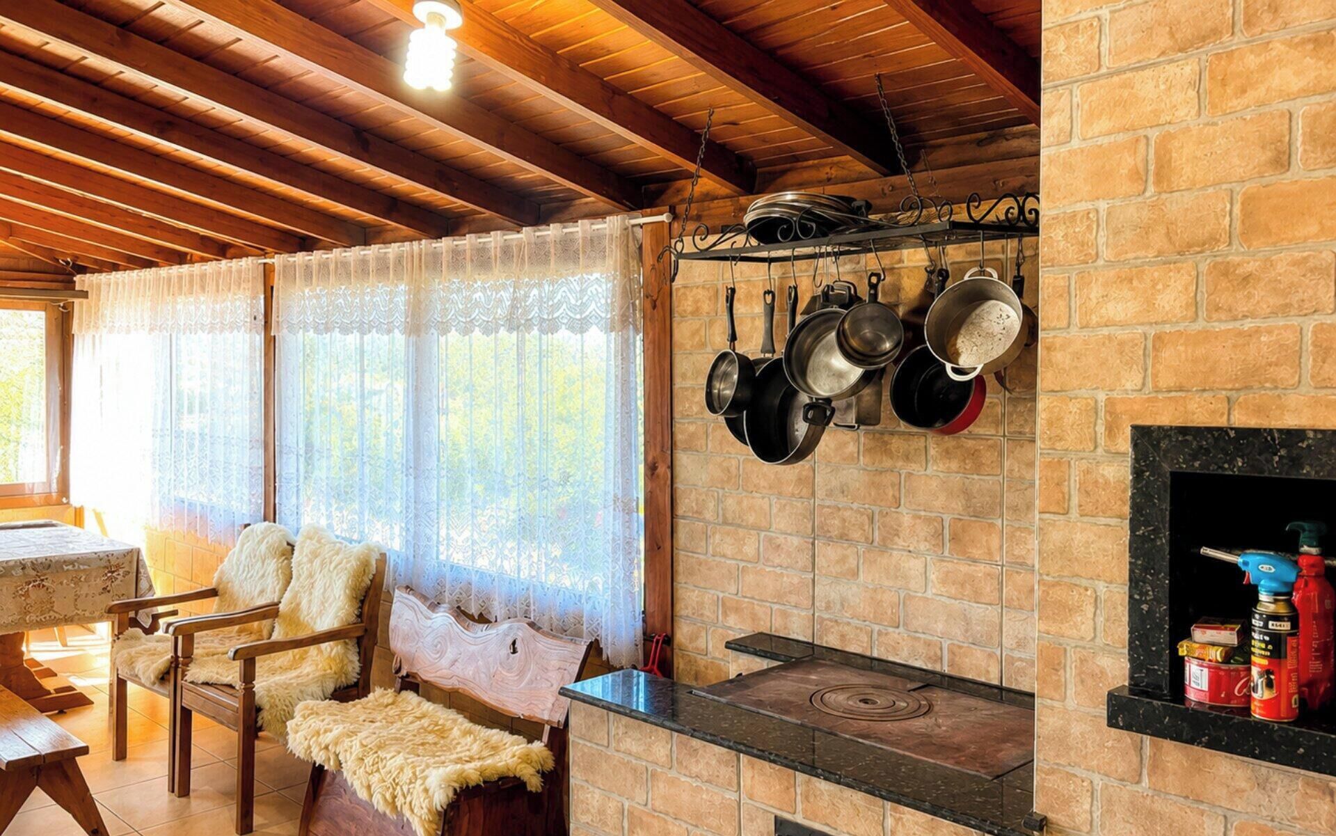 A rustic kitchen with a brick wall, hanging pots, a wooden ceiling, and a table with chairs.
