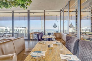Ein Restaurant mit hohen Decken, großen Fenstern und Blick auf die Stadt.