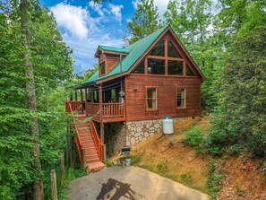 Eine Holzhütte mit Steinunterbau, einer Holzterrasse und einer Treppe, die zu einem Balkon im zweiten Stock führt.