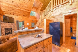 Ein Blockhaus-Interieur mit Kamin aus Stein, einer Holzauslage und einem Kühlschrank.