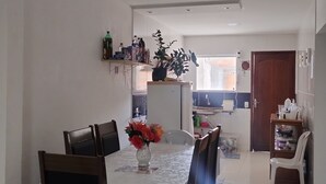 Een eetruimte met een tafel voor vier personen, stoelen, een vaas met bloemen en een keuken op de achtergrond.