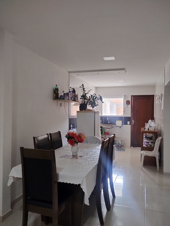 A dining area with a table set for four, chairs, a vase with flowers, and a kitchen in the background.