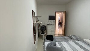 Een slaapkamer met twee bedden, een bureau, een stoel, een televisie en een spiegel.
