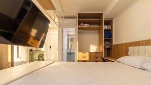 Habitación de hotel con cama, televisor montado en la pared, armario de madera y kitchenette.