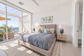 Ein Schlafzimmer mit einem großen Bett, Meerblick, Deckenventilator und einem Nachttisch mit Lampe.