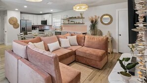Uma sala moderna com um sofá modular, uma área de jantar e uma cozinha ao fundo.
