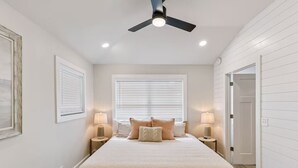 Quarto com cama, duas luminárias de cabeceira, ventilador de teto e janela com persianas.