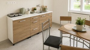 Cozinha moderna com armários brancos, fogão a gás, pia e área de jantar com mesa e cadeiras.