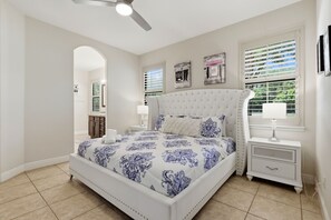 Un dormitorio con cama, mesitas de noche, ventilador de techo y ventana con persianas.