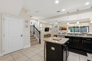 A modern kitchen with a central island, black cabinetry, and a staircase leading to another level. - Enchanted Pines Retreat!  Near Disney with Resort Pool (Davenport)