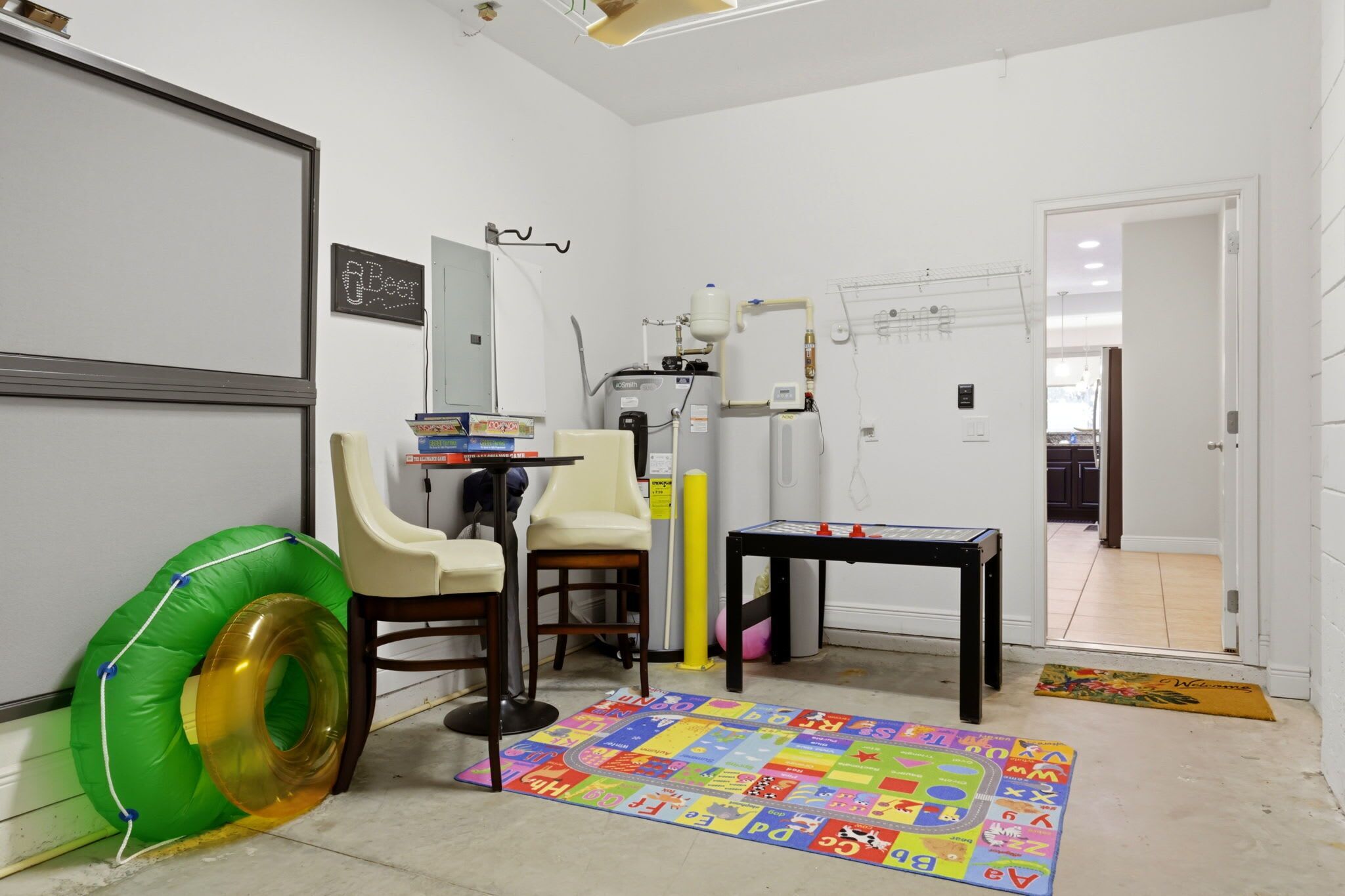 Ein Zimmer mit einer Tafel, einem Durchlauferhitzer, einem Stuhl, einem Tisch und einer bunten Spielmatte.