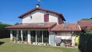 A two-story house with a covered patio, a water tank, and potted plants. - Basque-style house with a 300 m2 garden, a sunny veranda, and a plancha (Anglet)