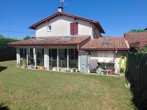 Ein zweistöckiges Haus mit überdachter Terrasse, einem Wassertank und Blumentöpfen.