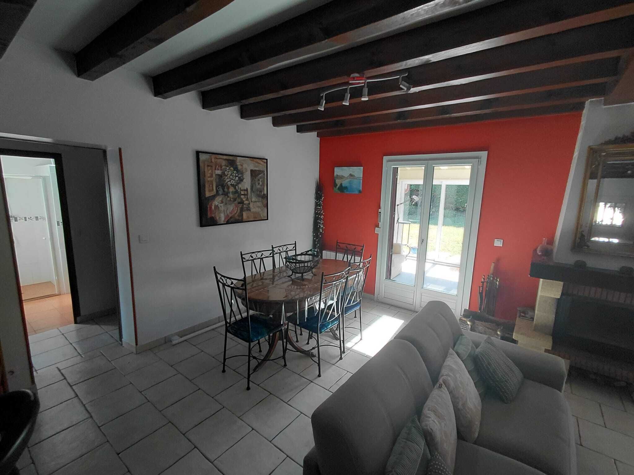 Un coin repas comprenant une table ronde et des chaises, un canapé et une porte-fenêtre coulissante donnant sur une terrasse.