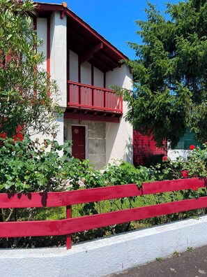 A two-story building with a red balcony, white walls, and a red fence in front. - Basque-style house with a 300 m² garden, a sunny porch, and a plancha (Anglet)