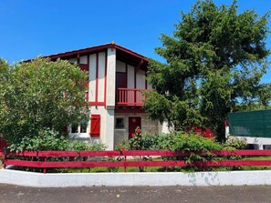 A two-story building with a balcony, surrounded by greenery and a red fence. - Basque-style house with a 300 m2 garden, a sunny veranda, and a plancha (Anglet)