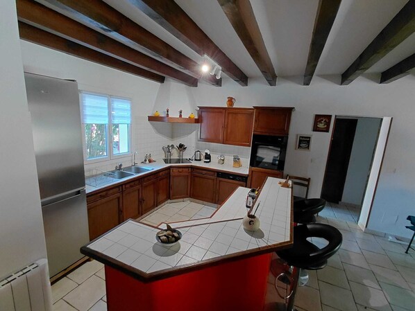 A kitchen with wooden cabinets, a stainless steel refrigerator, a tiled backsplash, and a red island counter. - Basque-style house with a 300 m2 garden, a sunny veranda, and a plancha (Anglet)