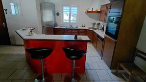 A kitchen with a red island, two bar stools, a refrigerator, a stove, and wooden cabinets. - Basque-style house with a 300 m2 garden, a sunny veranda, and a plancha (Anglet)