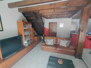 A living room with a television, a wooden cabinet, a brown leather sofa, and a staircase. - Basque-style house with a 300 m2 garden, a sunny veranda, and a plancha (Anglet)
