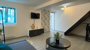 A modern living room with a sofa, a round coffee table with a plant, a TV on the wall, and a staircase.