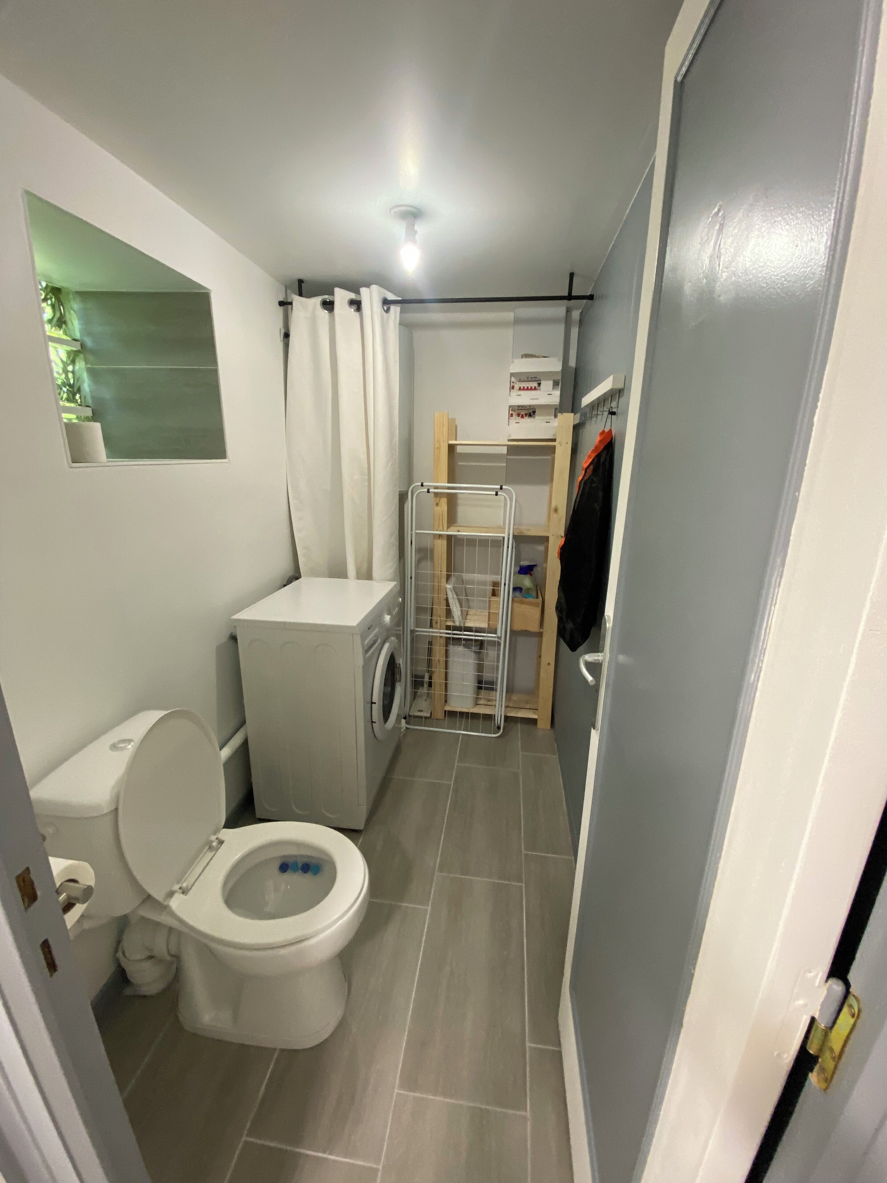 Un baño funcional con inodoro, lavadora y un pequeño estante.