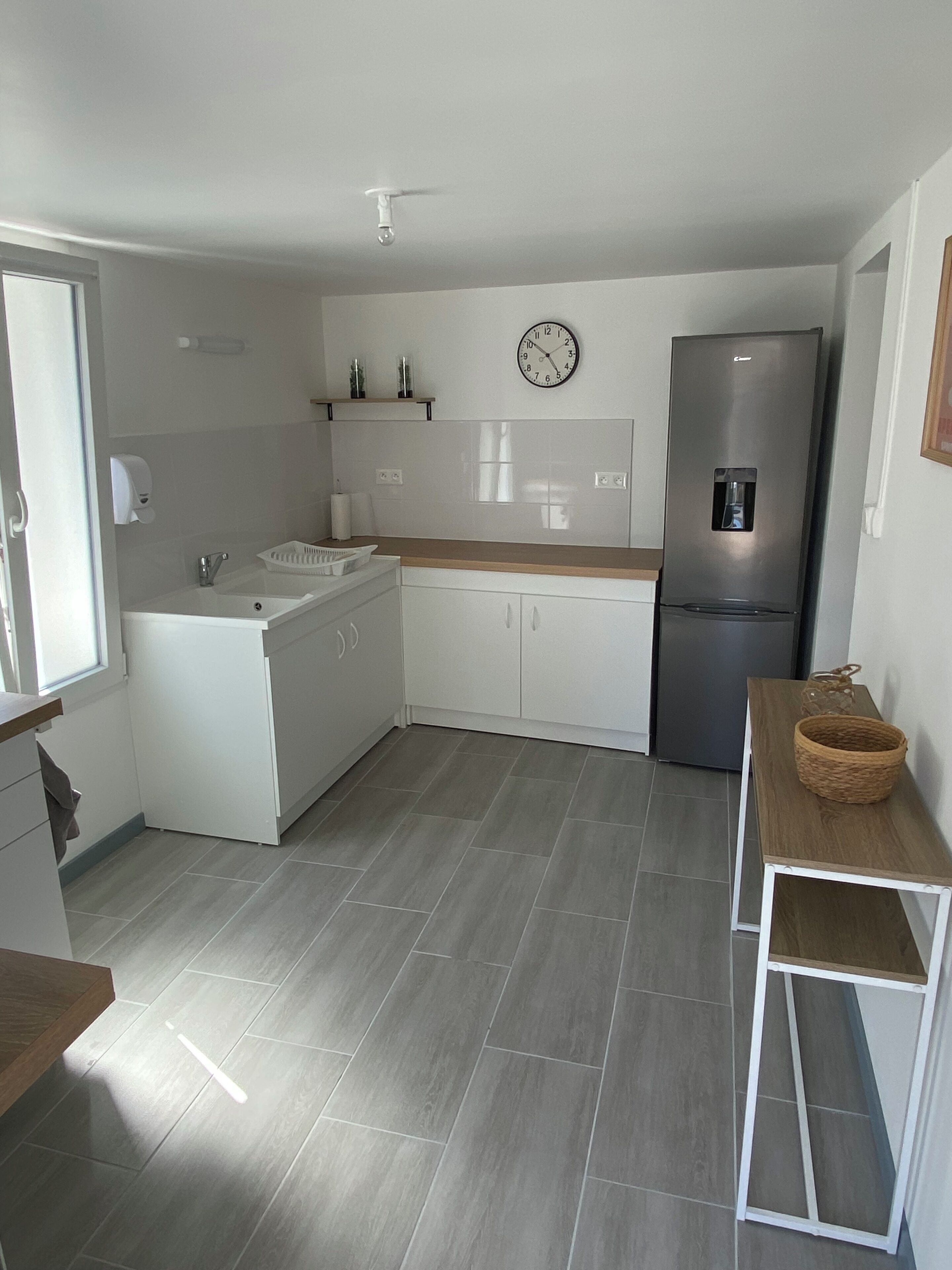 A compact kitchen with white cabinets, a built-in sink, a stainless steel refrigerator, and a wooden countertop.