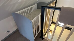 A room with a white crib, a blue wall, and a staircase with a black railing.