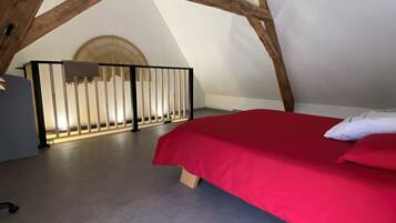 Una camera da letto mansardata con soffitto spiovente, travi in legno, un letto rosso e una ringhiera bianca.