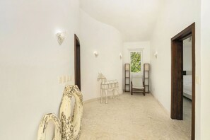 A narrow hallway with a white wall, a wooden door, a bed visible through the door, and a small window with a view of greenery. - Air Conditioning in the Living Room • Private Pool • Modern (Sosúa)