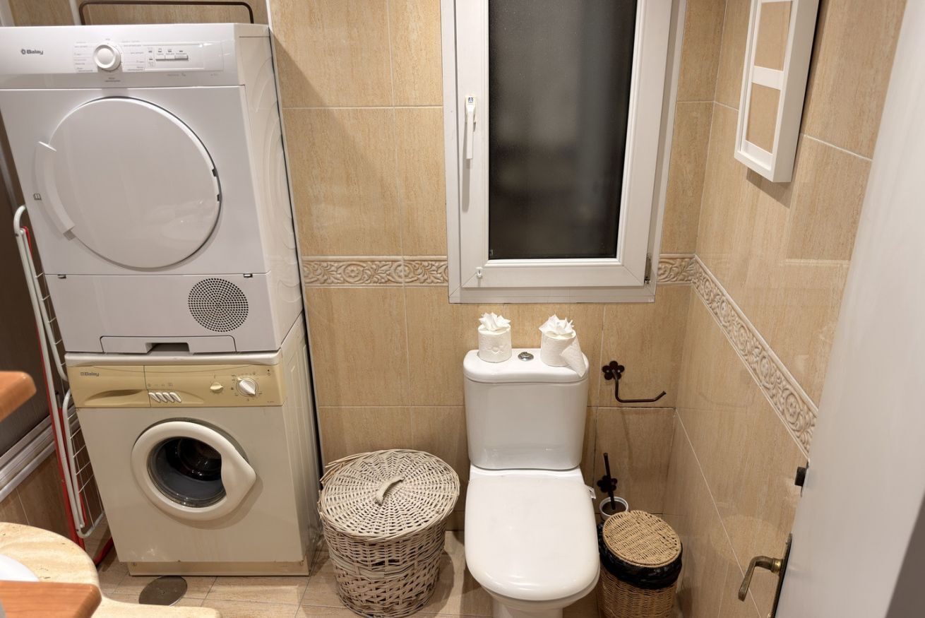 A compact bathroom with a washing machine, toilet, and two wicker baskets.