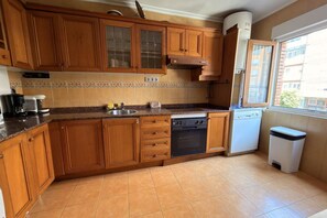A kitchen with wooden cabinets, a dishwasher, a stove, and a window. - 1A171 CBM Gijón: Apartment near the beach (Gijón)