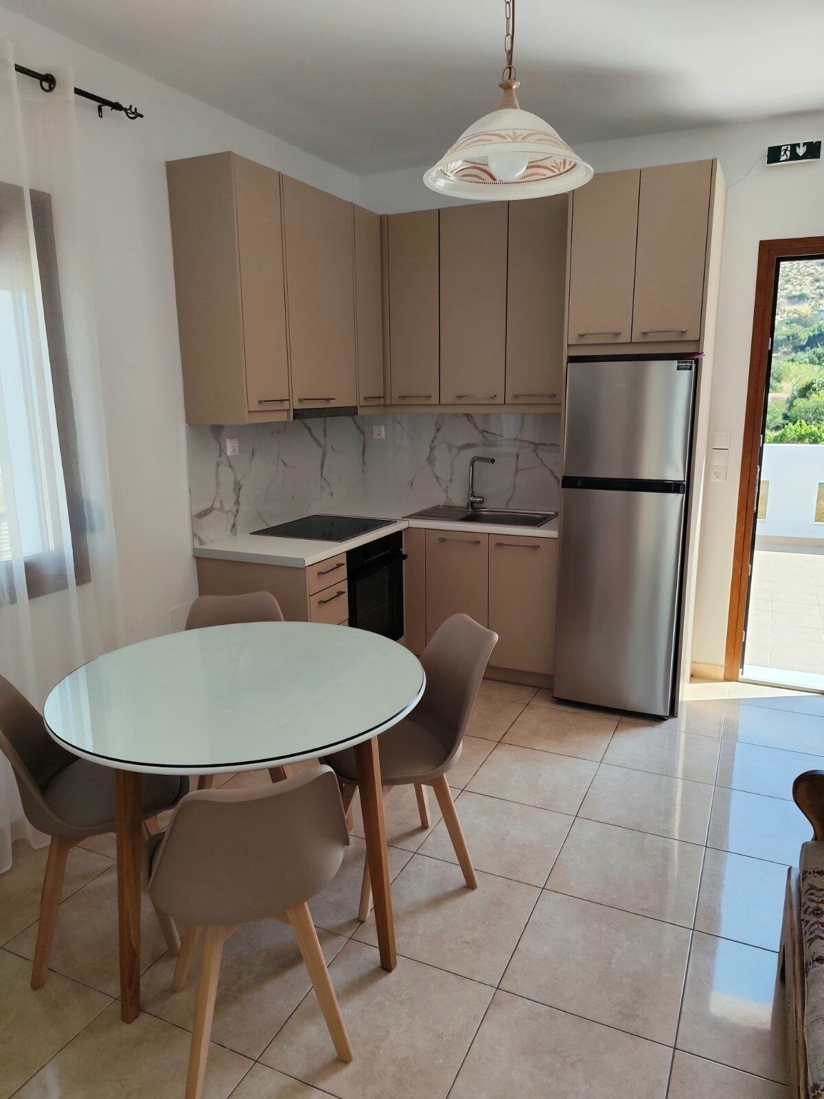 A modern kitchen with a round dining table, beige cabinets, a stainless steel refrigerator, and a pendant light.
