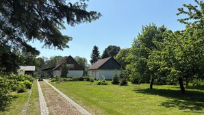 A rural setting with a paved path leading to a row of buildings, surrounded by greenery and trees. - Vacation Home Surrounded by Nature on Lake Kummerow (Dargun)