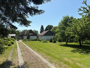 A rural setting with a paved path leading to a row of buildings, surrounded by greenery and trees. - Vacation Home Surrounded by Nature on Lake Kummerow (Dargun)