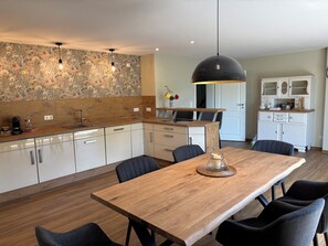 A modern kitchen with wooden cabinets, a dining table, and a pendant light. - Vacation Home Surrounded by Nature on Lake Kummerow (Dargun)