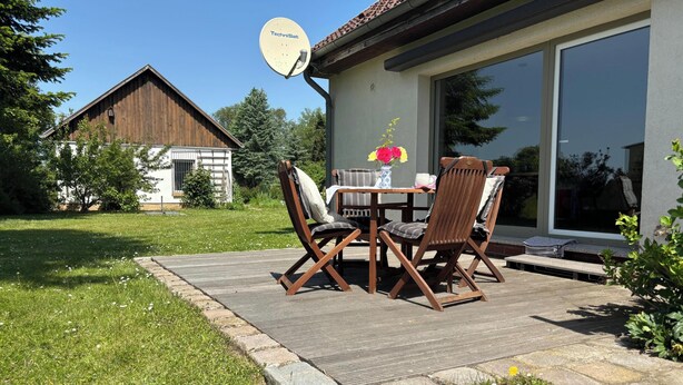 A patio with a table and chairs, a satellite dish, and a large window. - Vacation Home Surrounded by Nature on Lake Kummerow (Dargun)
