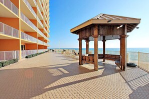 Ein Promenadweg am Strand mit einer hölzernen Laube, einem Poolbereich und einem Gebäude mit Balkonen.