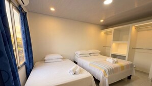 A hotel room with two beds, a window with curtains, a built-in wardrobe, and a ceiling light. - 7 colors available / AC / Airport pickup (San Andrés)