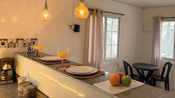 A kitchen with a countertop, a coffee maker, a fruit bowl, and a dining area with chairs and a table. - 7 colors available / AC / Airport pickup (San Andrés)